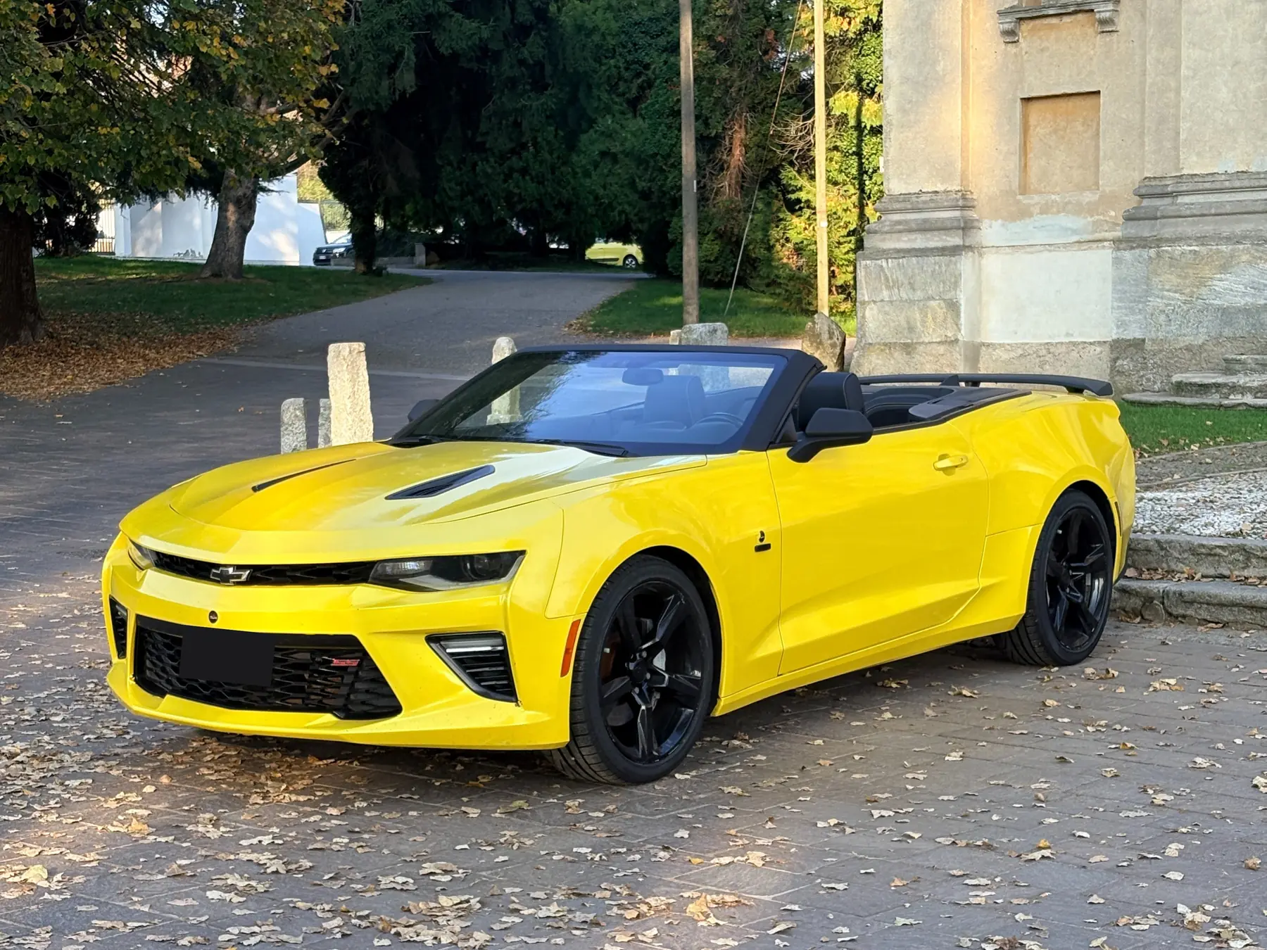 Chevrolet Camaro cabrio gialla di tre quarti su un piazzale con le foglie