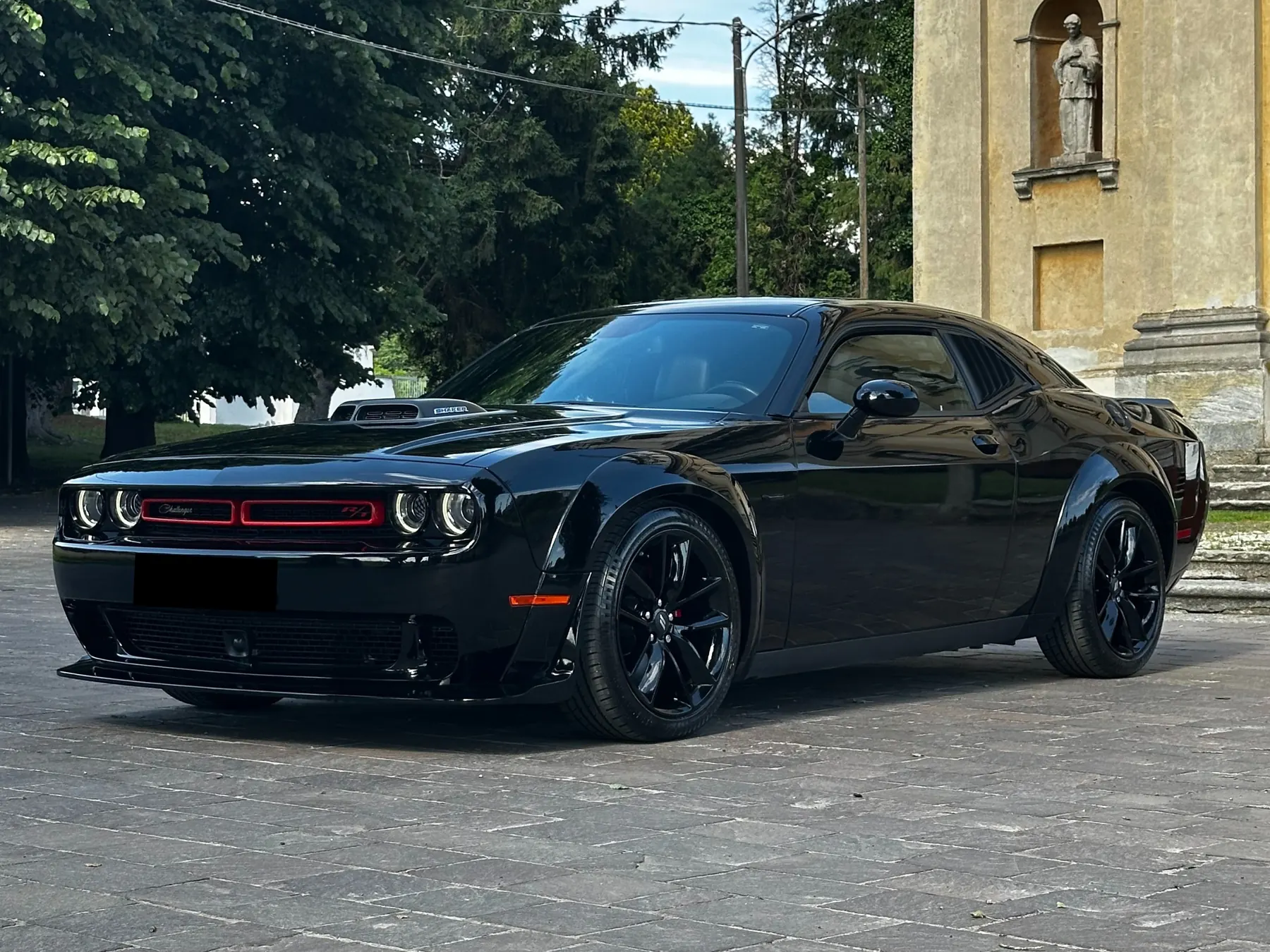 Dodge Challenger nera di tre quarti su un piazzale in pietra davanti a una chiesa