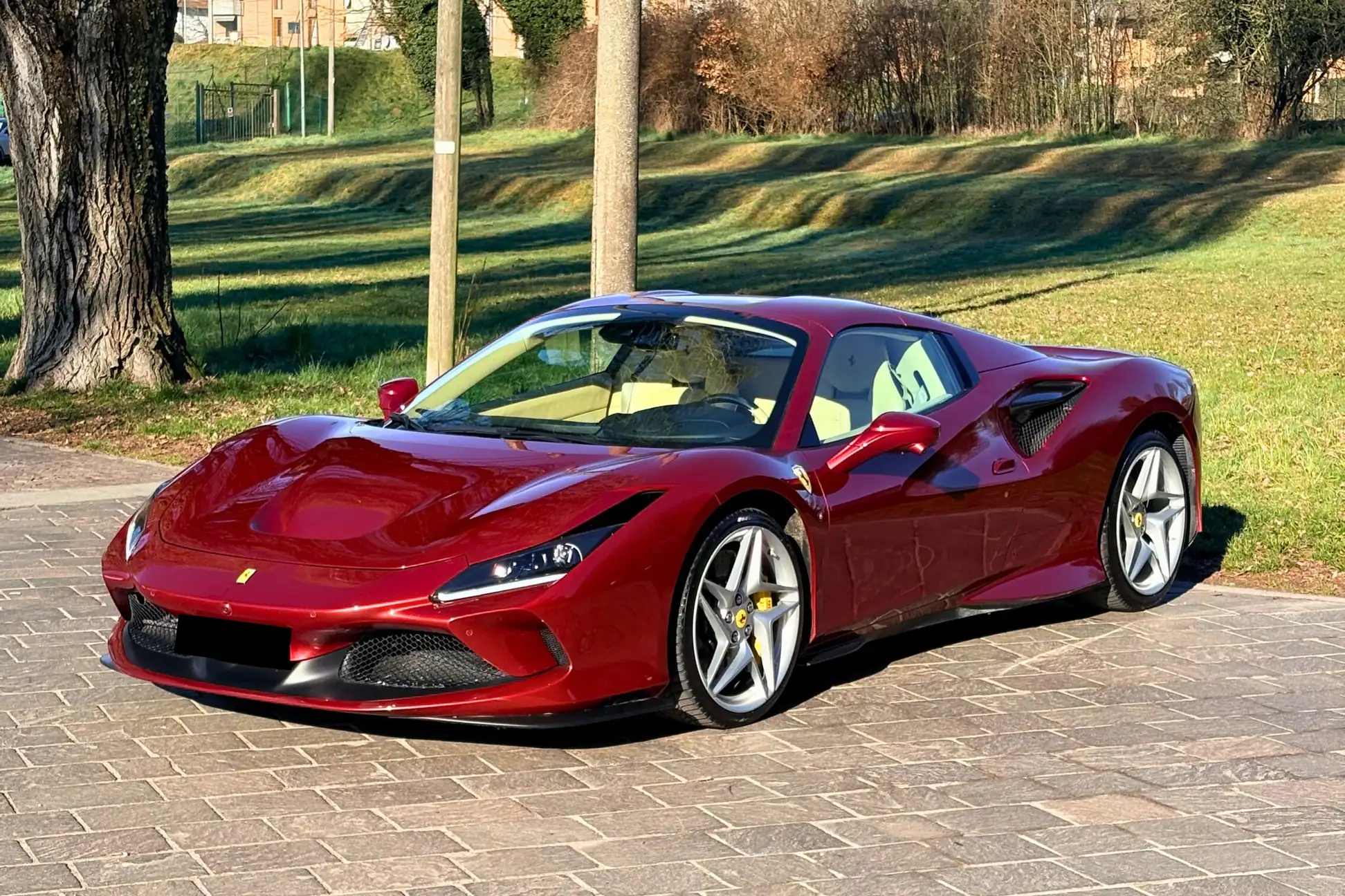 Ferrari F8 Spider rossa vista di tre quarti su un piazzale in pietra, con il prato e gli alberi dietro