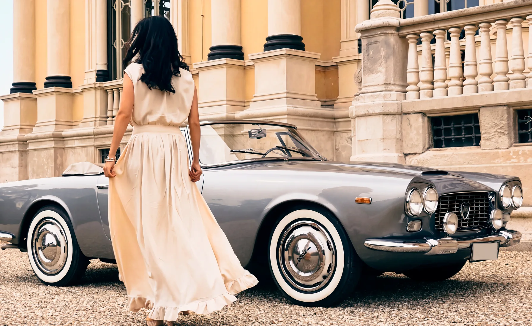Una donna in abito lungo, di spalle, si avvicina a una Lancia Flaminia cabriolet davanti al colonnato di una villa