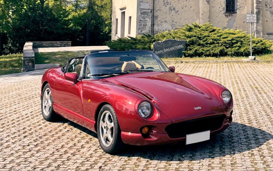Una TVR Chimaera rossa scoperta, vista di tre quarti su un piazzale in pietra davanti a un edificio antico