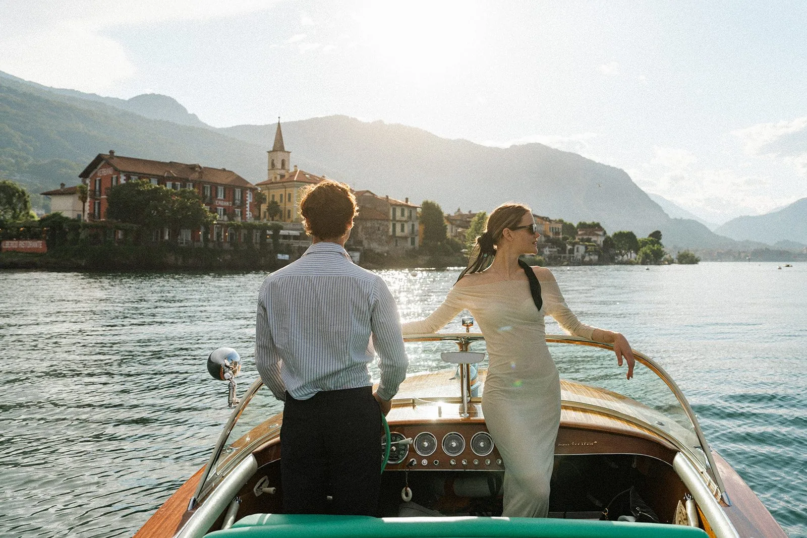 Due sposi di spalle a bordo di un Riva classico fermo davanti a un’isola del lago, nella luce del pomeriggio